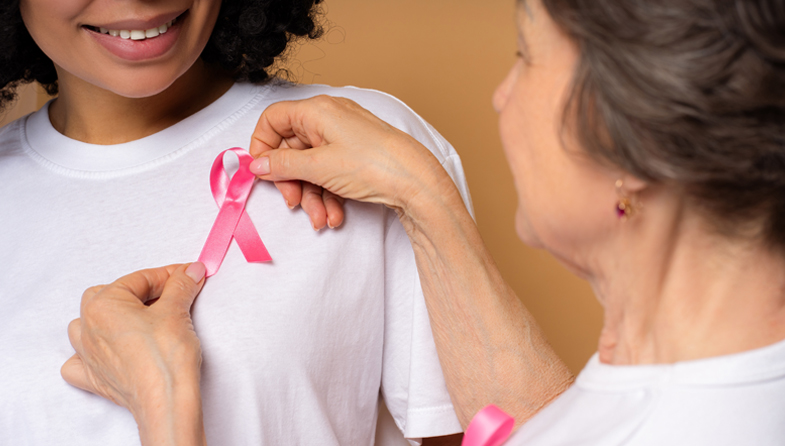 older woman pinning pink breast cancer awareness ribbon to younger woman's shirt