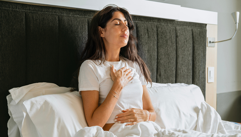 woman sitting in bed with hand on chest