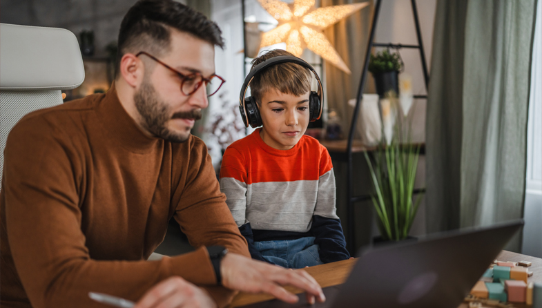 Man and child wearing headphones looking at laptop together