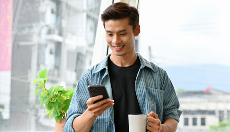 man looking at mobile phone and holding a cup of coffee