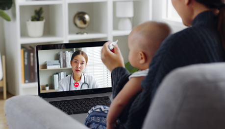 parent with baby in lap holding thermometer consulting doctor via computer meeting